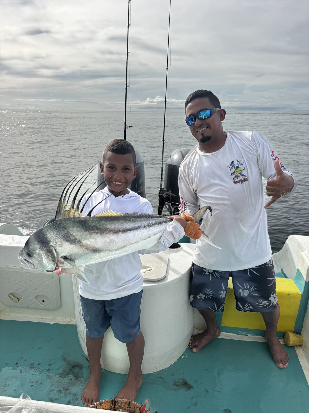 A boy holding a roosterfish next to the captain